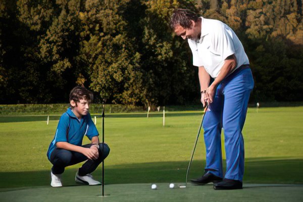 Kind lernt vom Golflehrer die Haltung