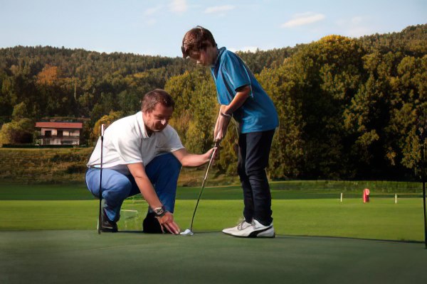 Kind beim Golfspielen vom Lehrer geführt